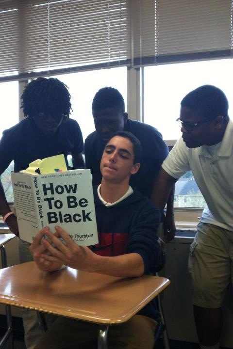 Photo d'un jeune blanc lisant un livre "comment être noir" entouré de 3 noirs