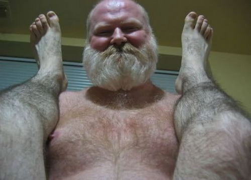 Photo d'un gros barbu en train de se faire photographier nu entre les jambes nues du photographe