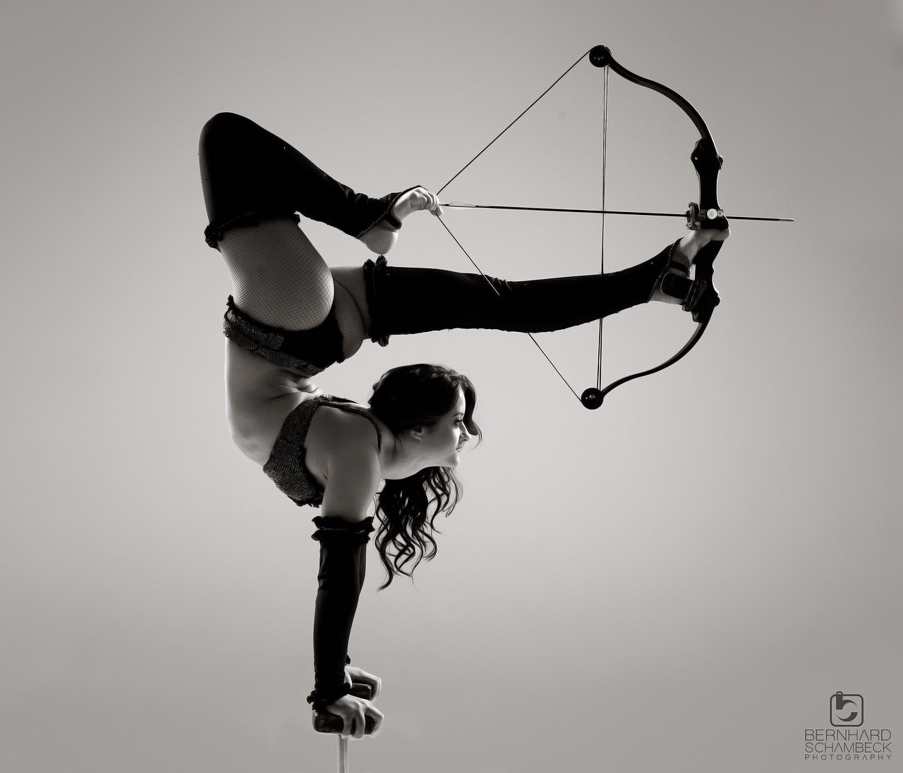 Photo d'une femme tirant à l'arc en équilibre sur les mains, l'arc dans les pieds